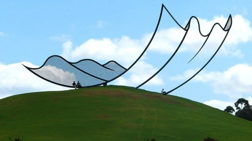 Moderná socha na kopci s modrou oblohou, abstraktné línie symbolizujú vlny alebo vietor.