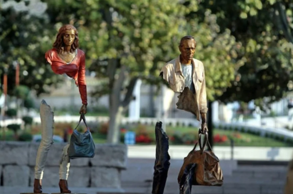 Sochy ľudí bez strednej časti tela držiacich tašky v parku s rozmazaným pozadím.