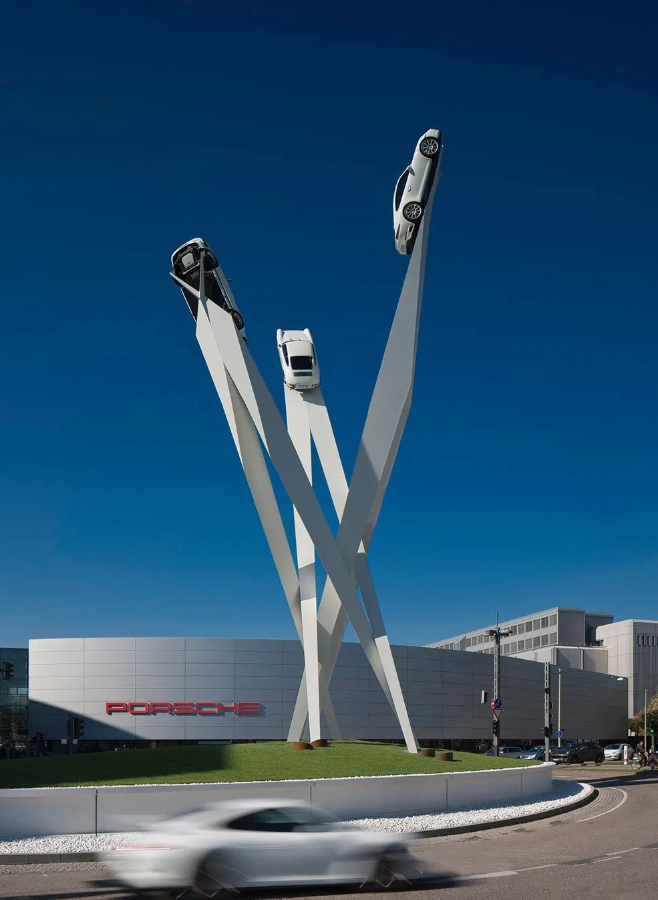 Tri modely Porsche vystavené na vysokých stĺpoch pred budovou výrobcu v Stuttgarte.