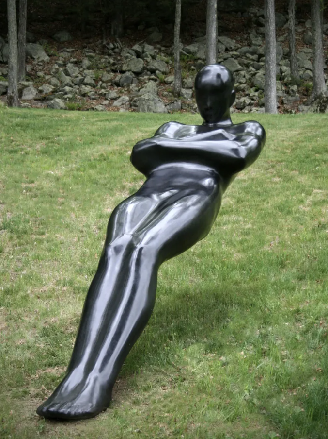 Ľudská socha v trávnatej záhrade, naklonená póza, čierny hladký povrch.