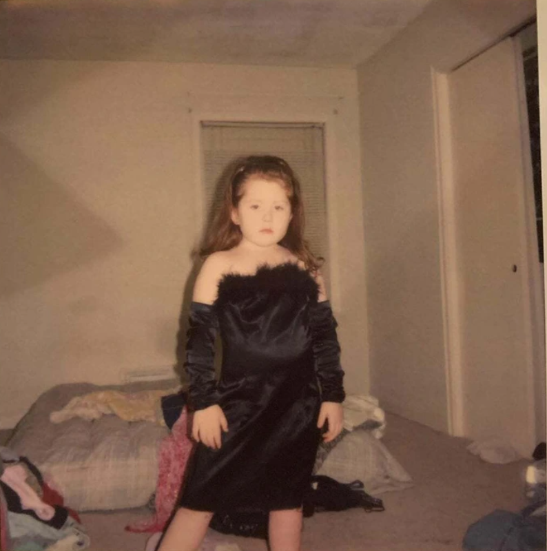 Dieťa v čiernych šatách stojí v miestnosti pri posteli, okolo neho sú rozhádzané oblečenie.