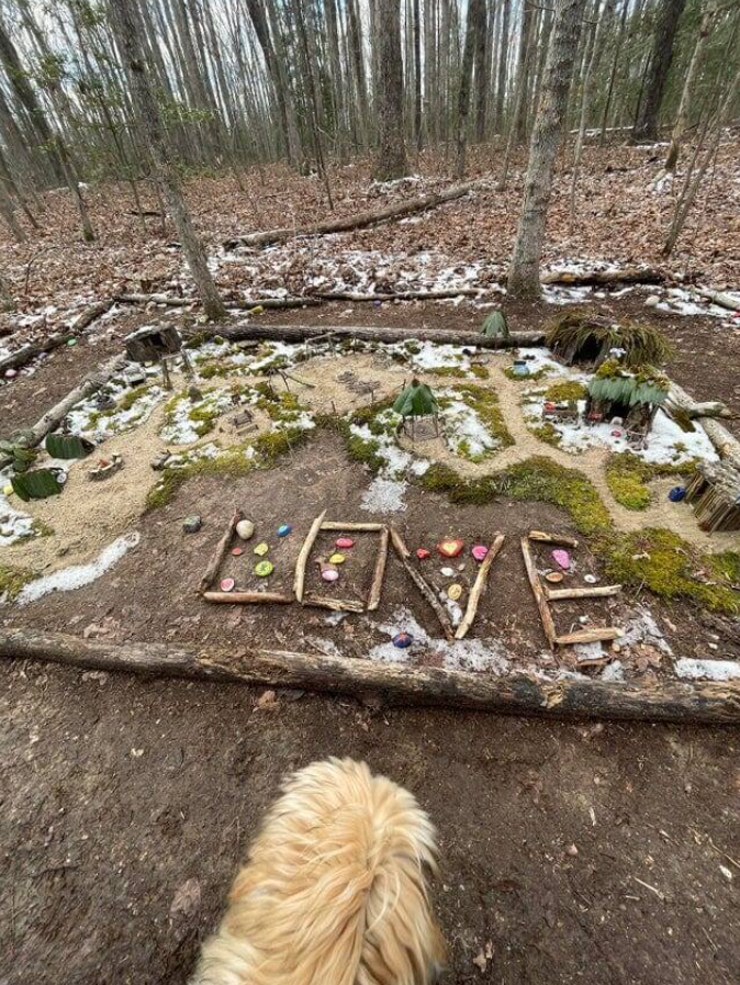 Lesná cesta s nápisom LOVE z vetvičiek a kameňov, okolo snehové škvrny a machové porasty.