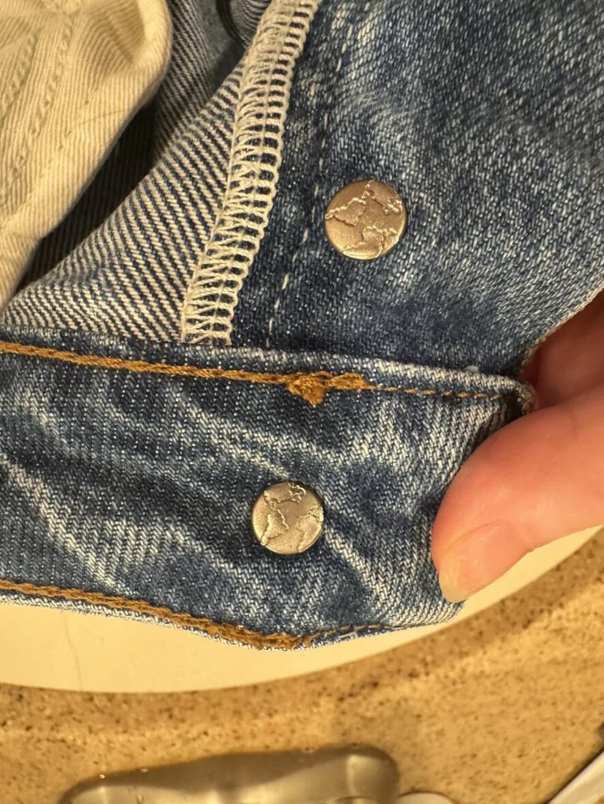 Džínové nohavice s kovovým gombíkom s motívom mapy sveta, detailný pohľad.