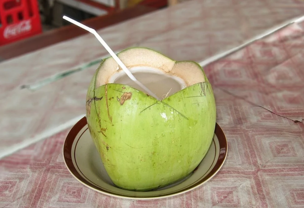 Čerstvý zelený kokos s brčekom na tanieri, ideálny na osviežujúce letné nápoje.