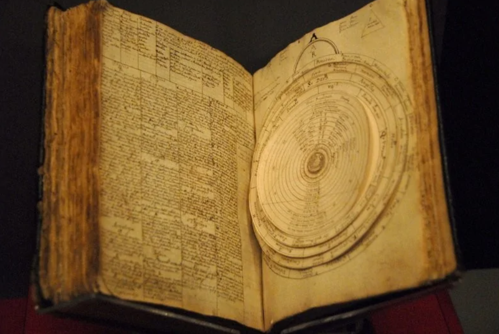 Stará kniha s historickými astronomickými diagramami a textom na opotrebovaných stránkach.