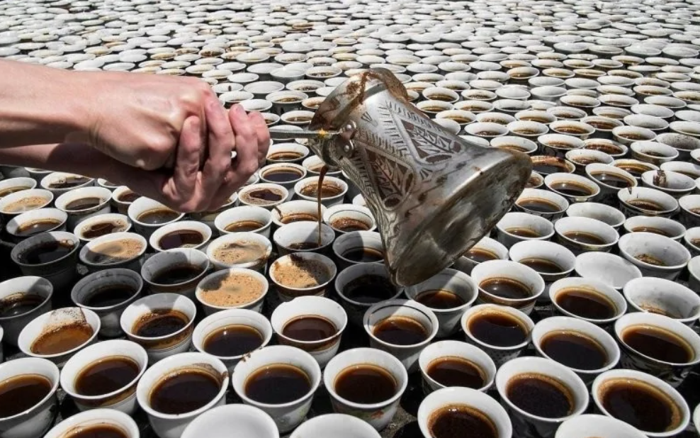Množstvo šálok kávy, do ktorých sa nalieva tekutina z tradičnej konvice, symbolizujúcej bohatý kávový zážitok.