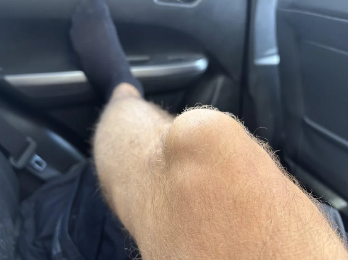 Koleno položené na palubnej doske auta počas jazdy, noha v čiernej ponožke opretá o okno.