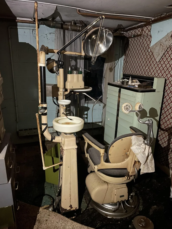 Starý zubársky kreslo v opustenom dome, obklopené retro vybavením a tmavým interiérom.