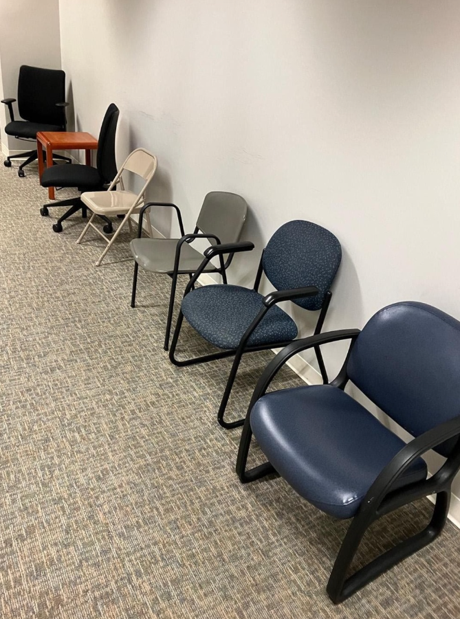 Rôznorodé kancelárske stoličky zoradené pozdĺž bielej steny na kobercovej podlahe.