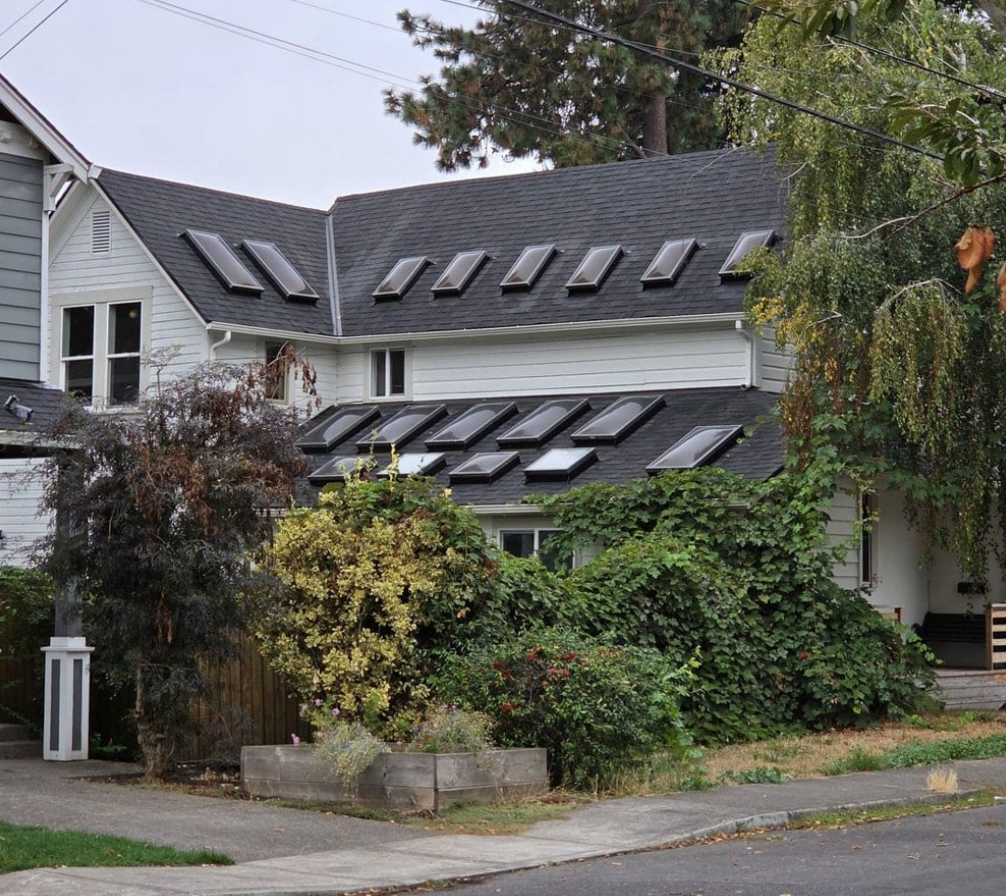 Biely dom so šikmou strechou a solárnymi panelmi, obklopený zeleňou na vidieckej ulici.