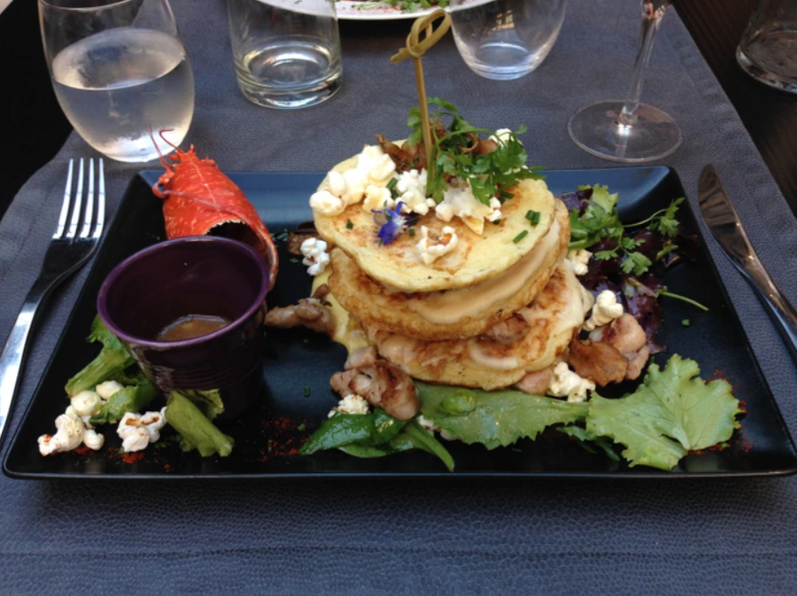 Luxusné jedlo na tmavom tanieri so šalátom a morským plodom, doplnené maslovými plackami a omáčkou.