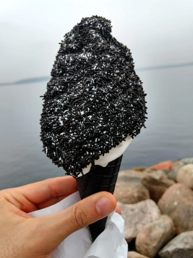 Čierna zmrzlina v kornútku s čiernymi posýpkami pri jazere.