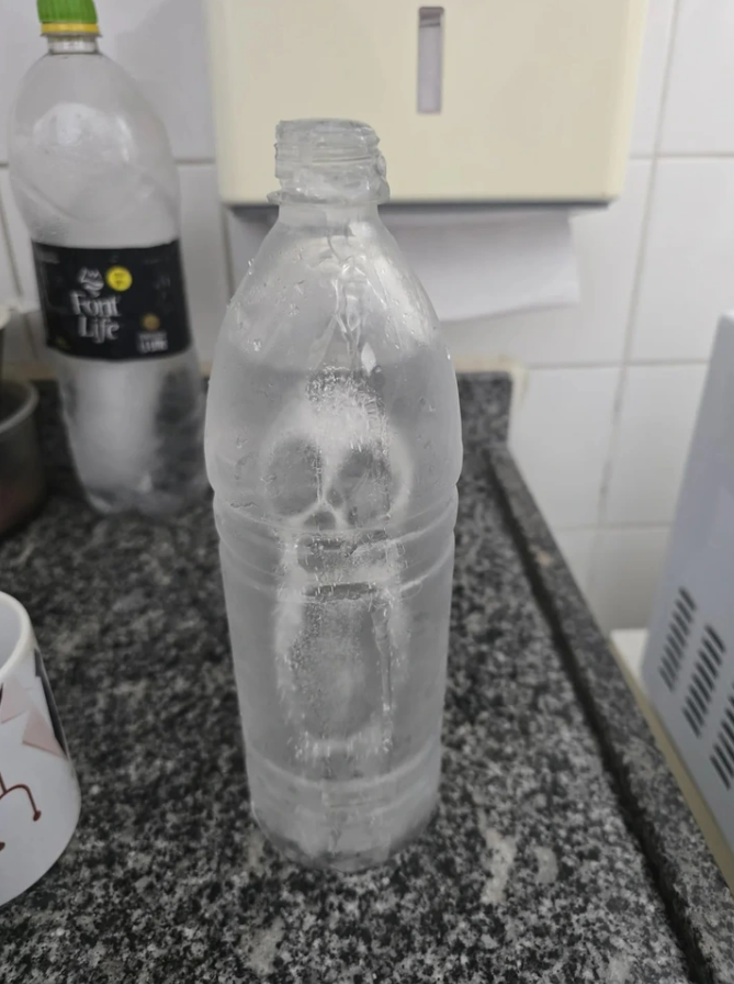 Mrazená fľaša so vzorom lebky na kuchynskej linke vedľa ďalšej fľaše a hrnčeka.