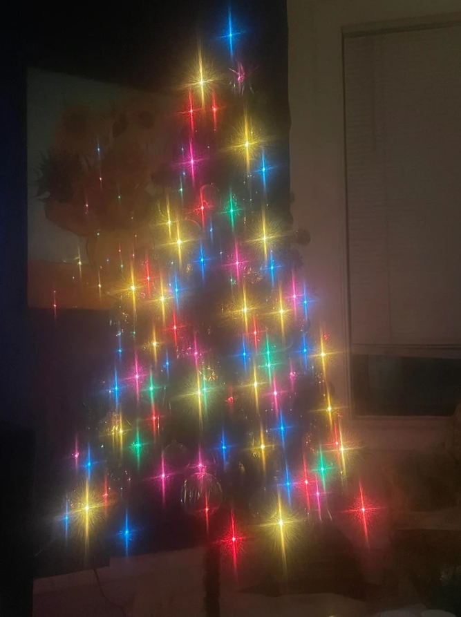 Farebne osvetlený vianočný stromček so žiarivými svetielkami v tmavej miestnosti.