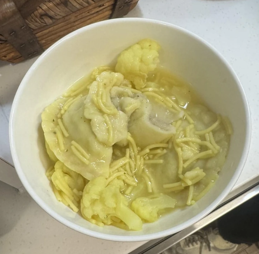 Miska s polievkou, obsahujúca cestoviny, varené cesto a karfiol, podávaná na bielej doske.