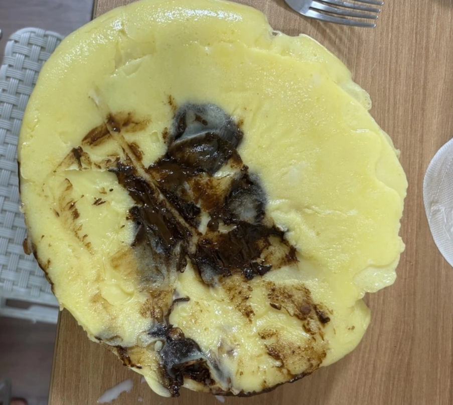 Nadýchaná palacinka s hnedými škvrnami na drevenom stole, vidlička a tanier vedľa.