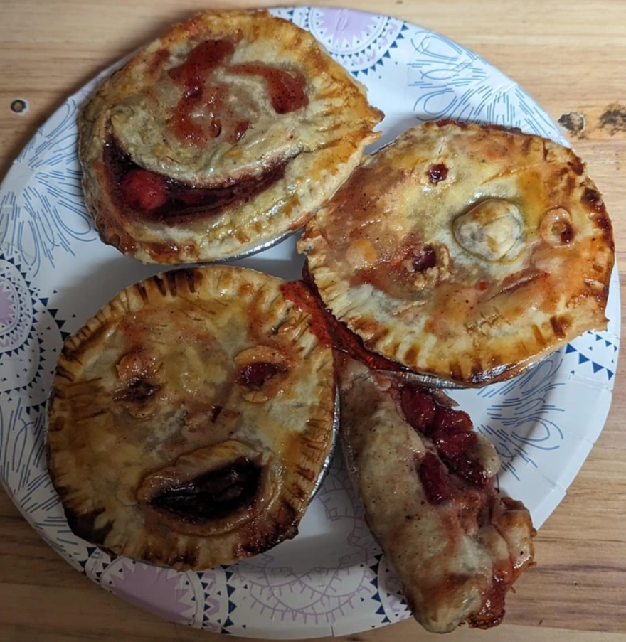 Štyri koláče s tvárami na tanieri, vytvarované z cesta a plnené marmeládou, usporiadané na drevenom stole.