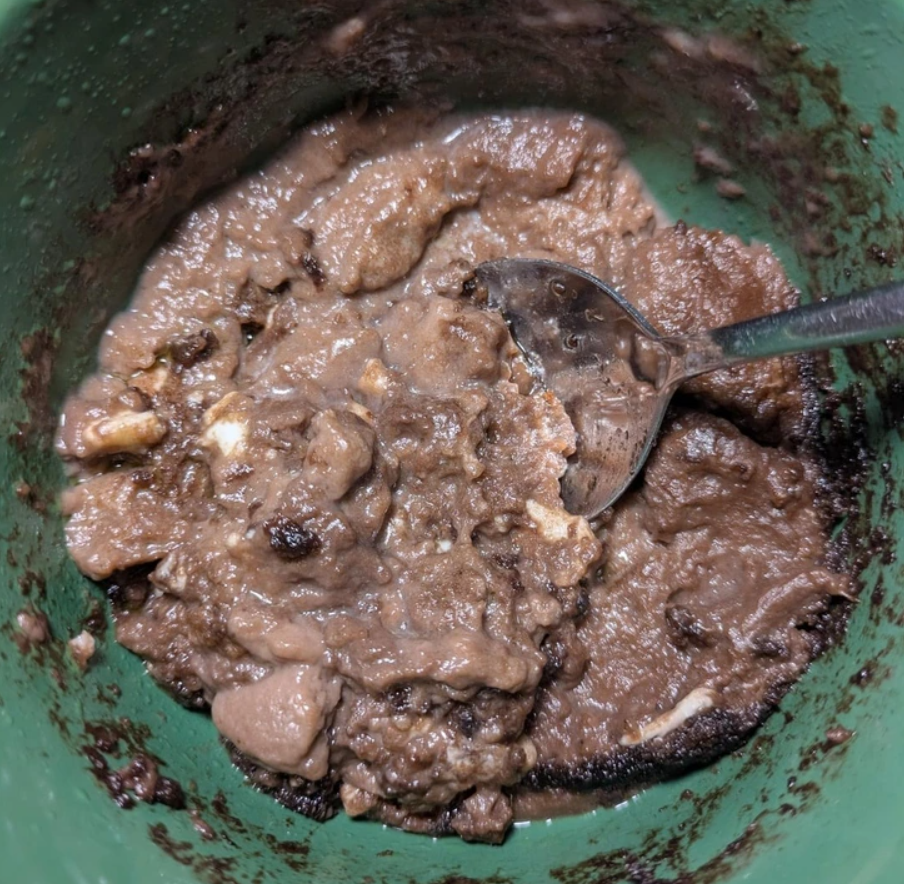 Hustá čokoládová kaša v zelenom hrnčeku s lyžicou, domáci dezert alebo raňajková pochúťka.