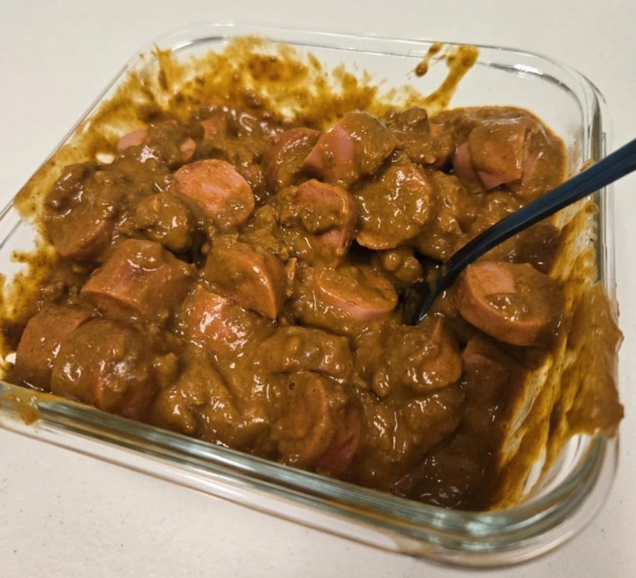 Kúsky párkov v hustej, tmavej omáčke podávané v sklenenej miske, s čiernou lyžičkou po pravej strane.