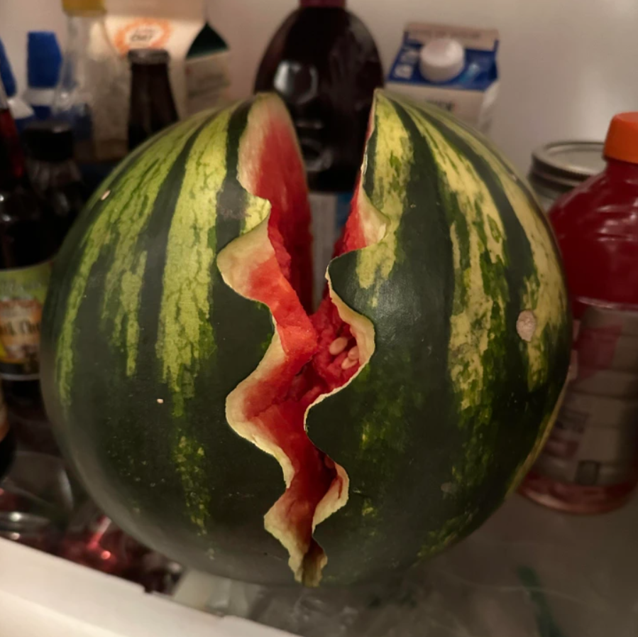 Prasknutý vodný melón v chladničke, odhalujúci červenú dužinu a semienka, s rôznymi nápojmi na pozadí.