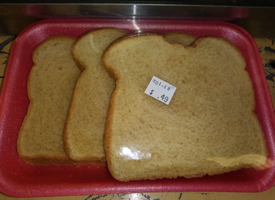 Plátky toastového chleba na červenom tácke s cenovkou 0,49 dolára pod plastovým obalom.