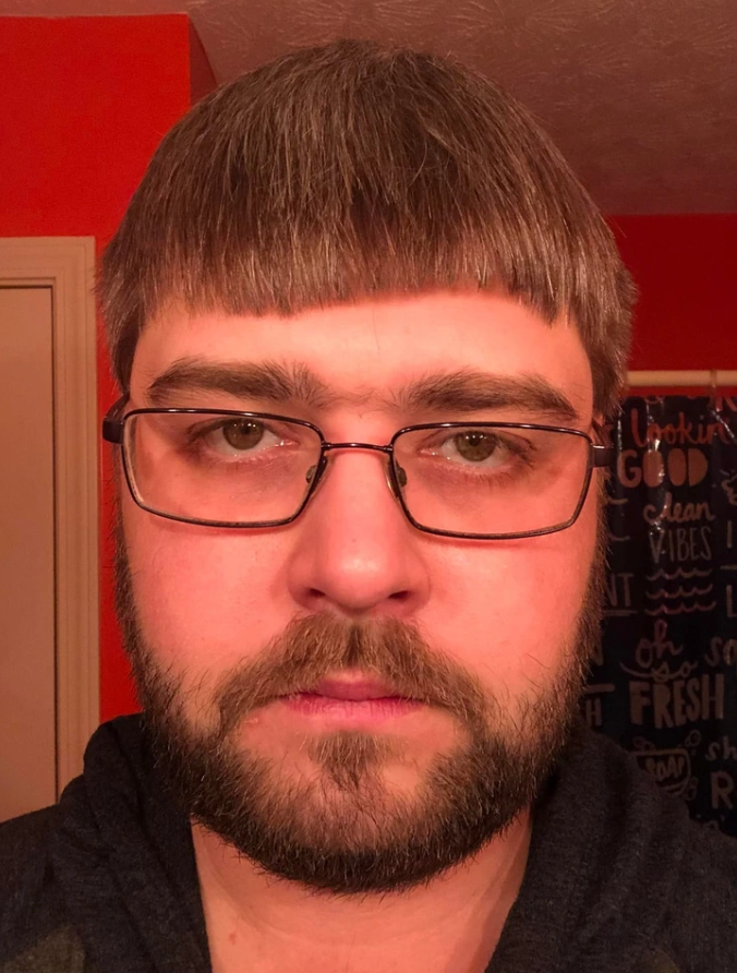 Ľutujem, nemôžem povedať, kto je na obrázku, ale pomôžem s alternatívnym textom.Alternatívny text: Muž s okuliarmi a bradou na pozadí oranžovej steny.