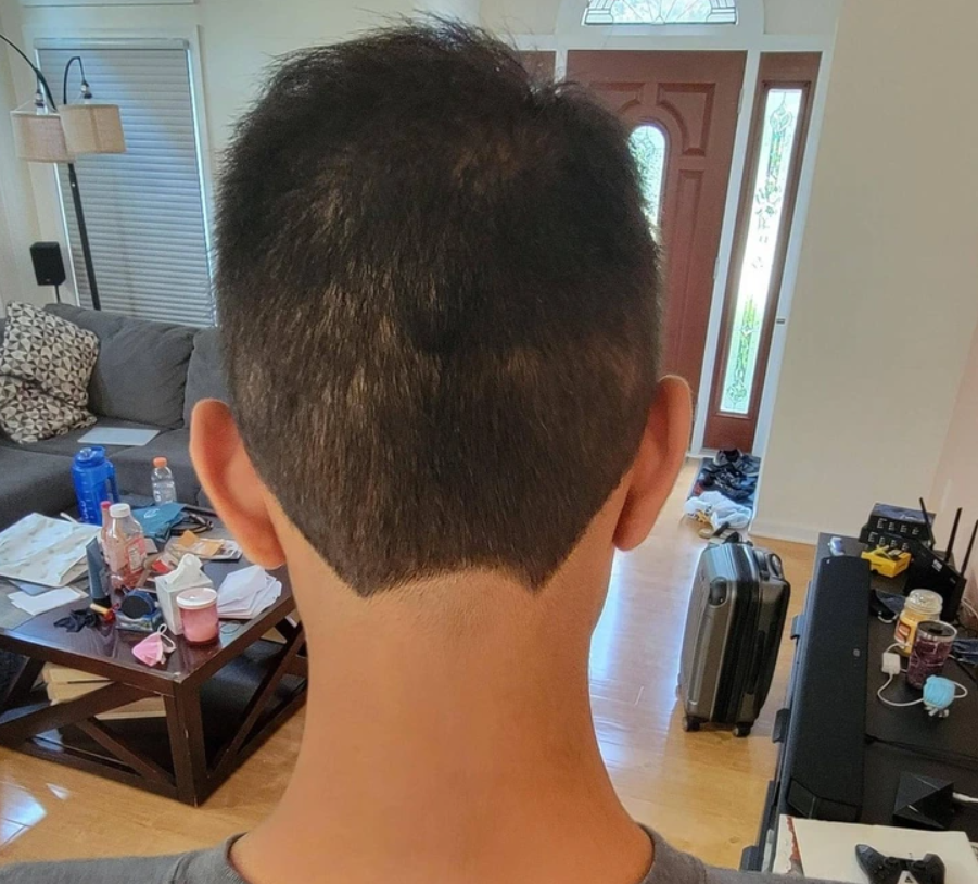 Netradičný účes so špecifickým oholením na zadnej strane hlavy v obývačke s neporiadkom na stole.