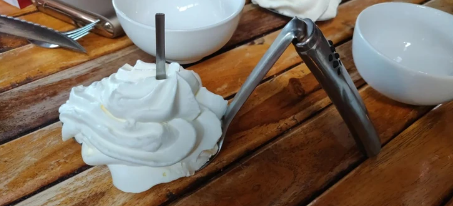 Šľahačka a drvič cesnaku na drevenom stole, v pozadí biele misky.