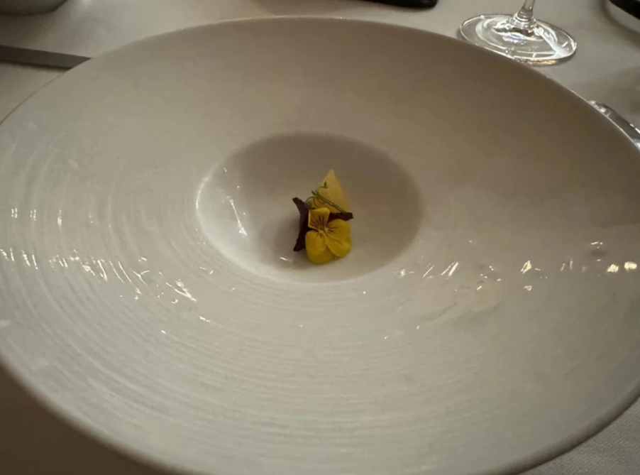 Biela tanier s elegantnou kvetinou uprostred, pripravená na servírovanie v luxusnej reštaurácii.