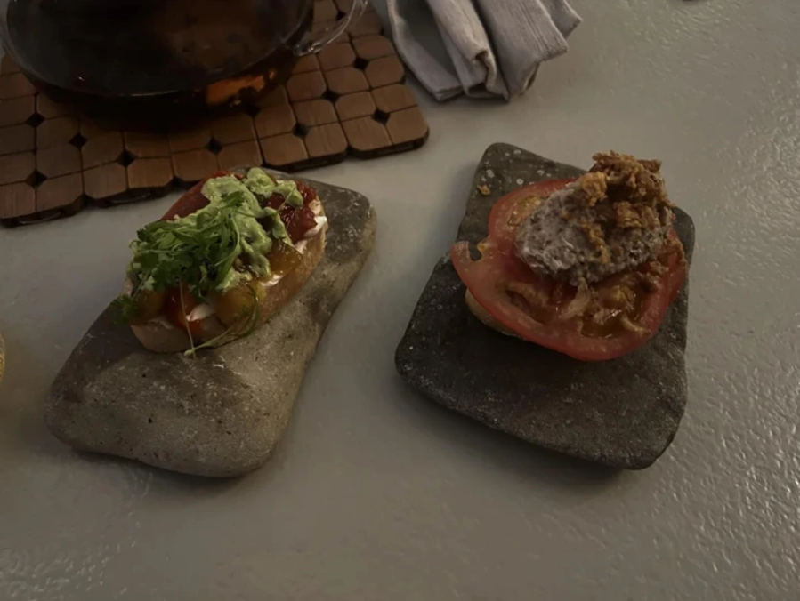 Dve bruschetty s pestrom obložením na kameni, dekorované bylinkami a paradajkami, podávané na elegantnom stole.