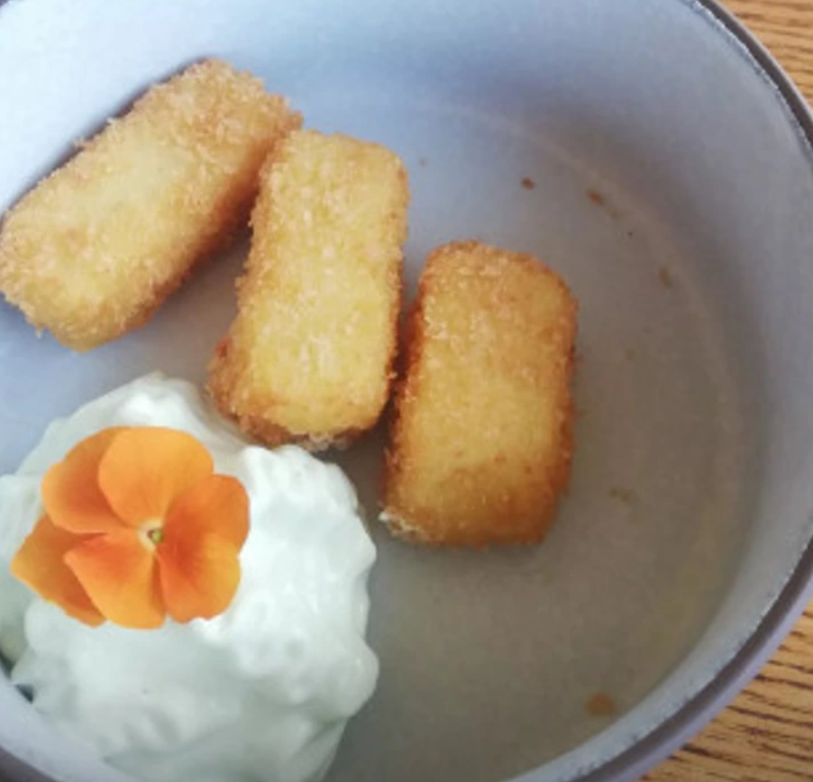 Tri vyprážané tyčinky s bielym krémom ozdobeným oranžovým kvetom podávané v keramickom tanieri.