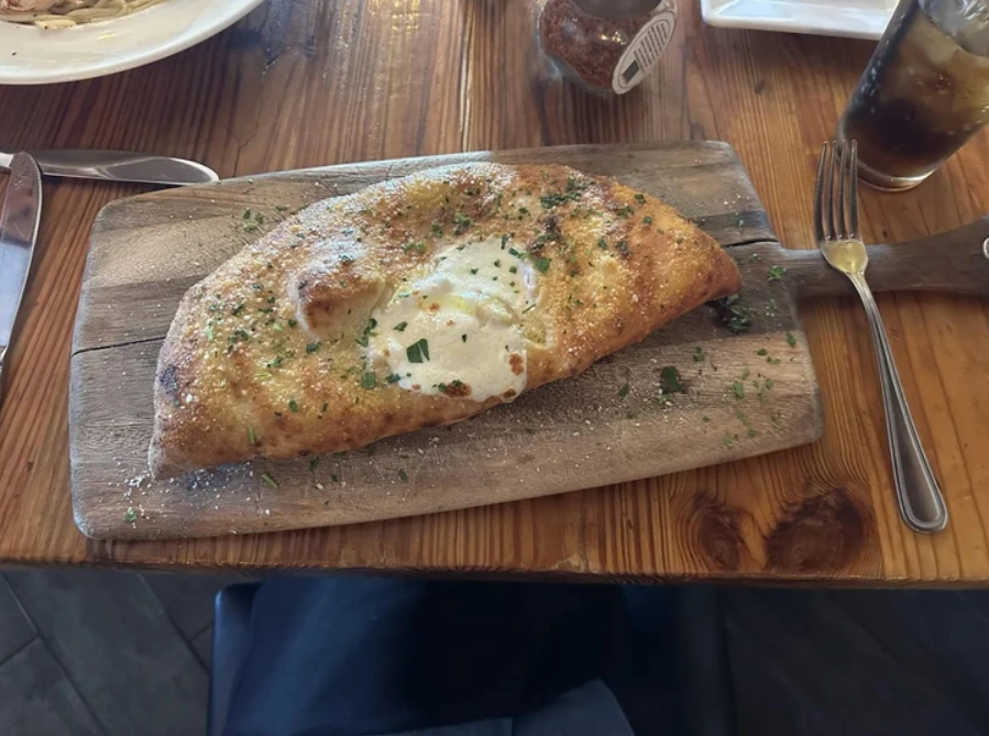 Pečená calzone na drevenej doske, ochutená bylinkami, pripravená na servírovanie v reštaurácii.