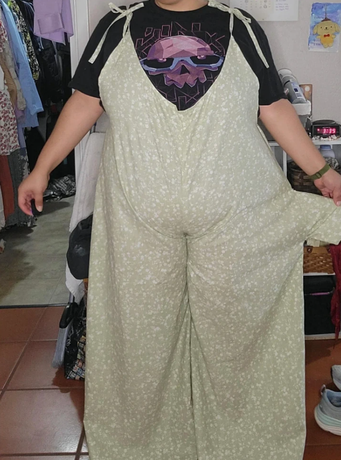 Osoba v kvetovaných nohaviciach ukazuje nadrozmerný odev vo vnútri izby.