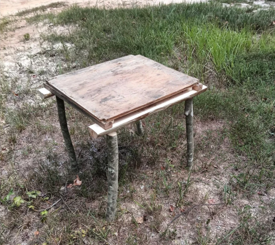 Drevený provizórny stolík s nepravidelnými nohami na trávale na vidieku.