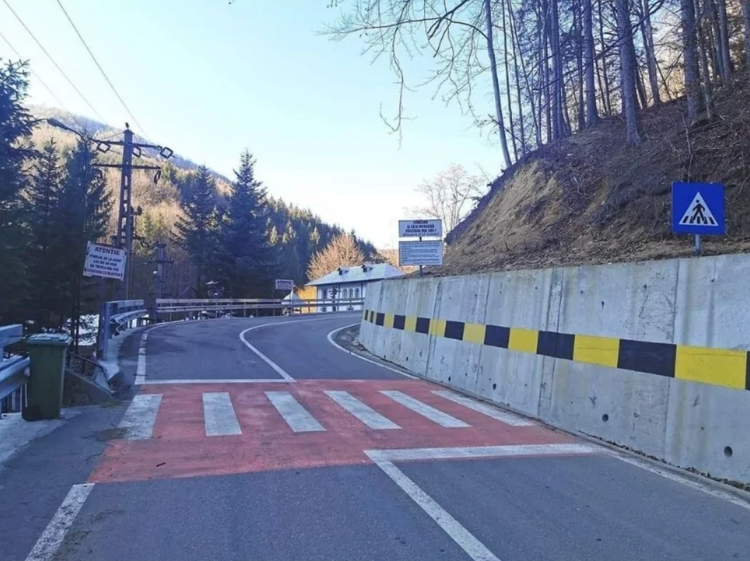 Horská cesta s priechodom pre chodcov, vedľa svahu a lesa, v zimnom období, označená viacerými dopravnými značkami.