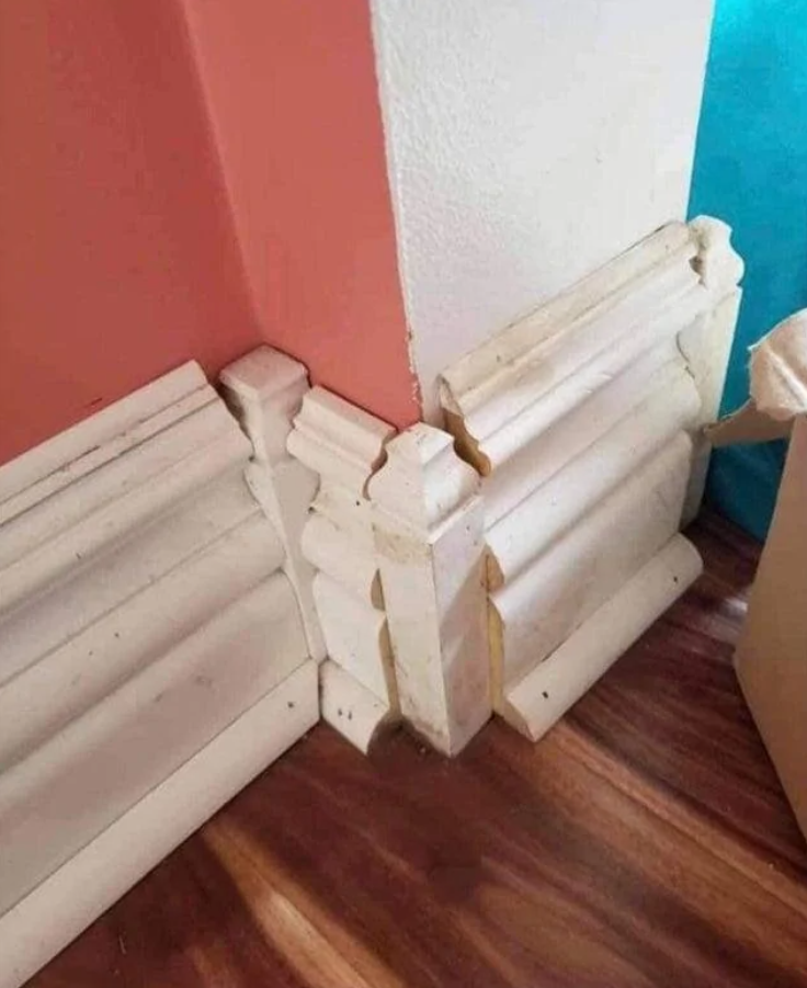 Nesprávne nainštalované dekoratívne lišty na rohu miestnosti s farebnými stenami a drevenou podlahou.