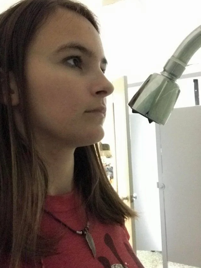 Osoba v červenom tričku zblízka vedľa veľkej sprchovej hlavice v interiéri.