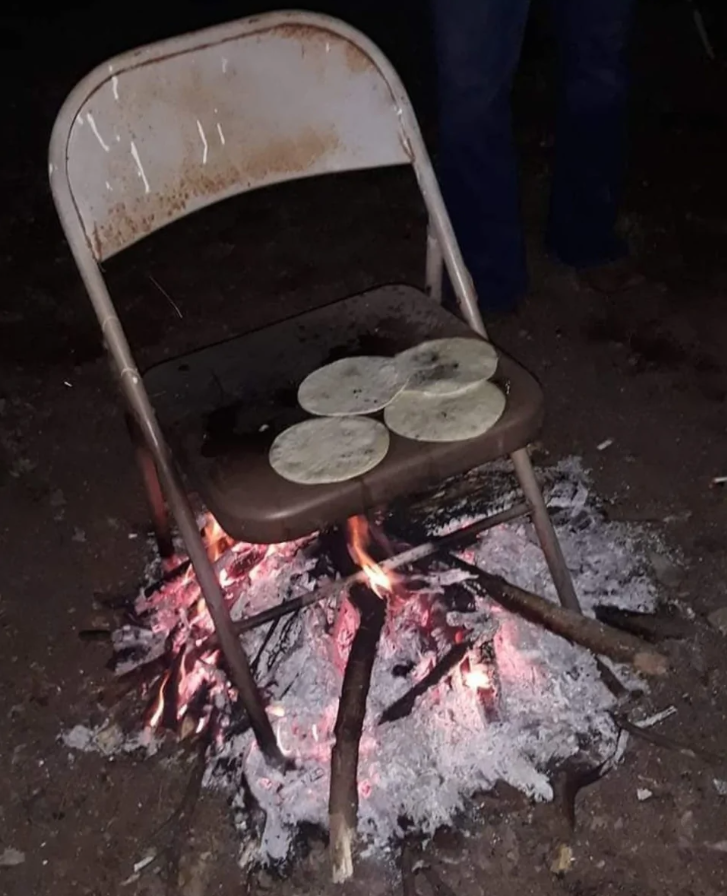 Stolička s tortillami položená nad ohniskom na otvorenom priestranstve v noci.