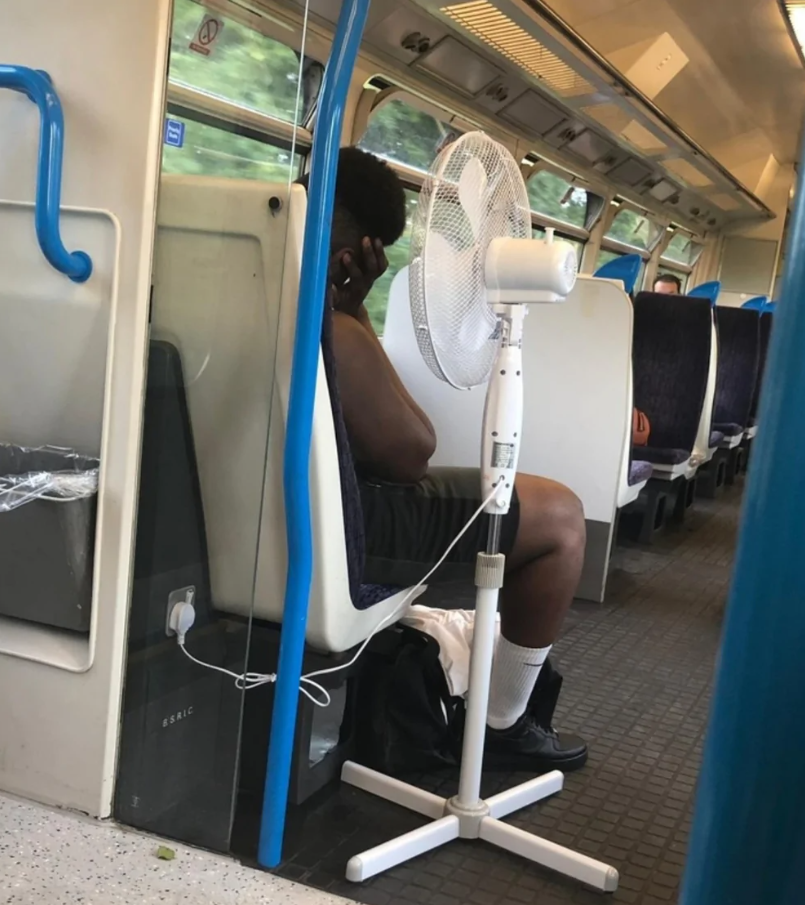 Cestujúci vo vlaku s prenosným ventilátorom na ochladenie počas jazdy.