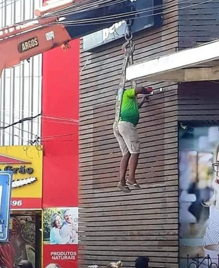 Muž vežou visí z budovy počas opravárenských prác v meste.