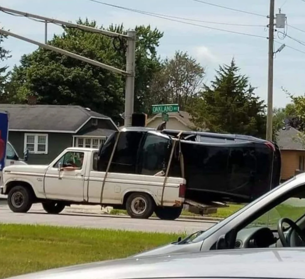 Pickup s neobvyklým nákladom auta pripevneného na streche, zastavený na križovatke.