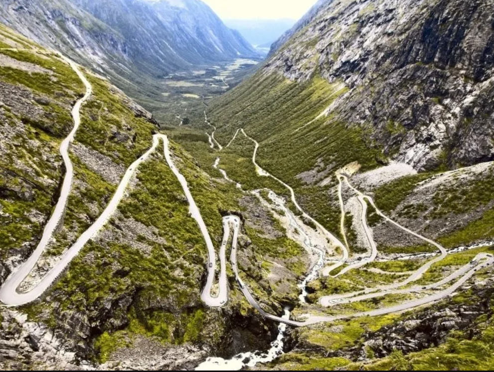 Serpentínová cesta v horskom údolí s bujnou zeleňou a dramatickými vrcholmi, ideálna pre dobrodružné výlety.