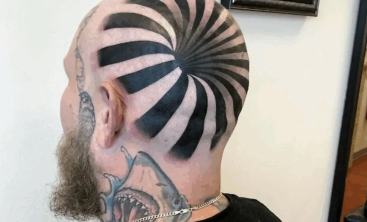 Muž s čierno-bielym špirálovým tetovaním na hlave a tetovaním žraloka na krku.