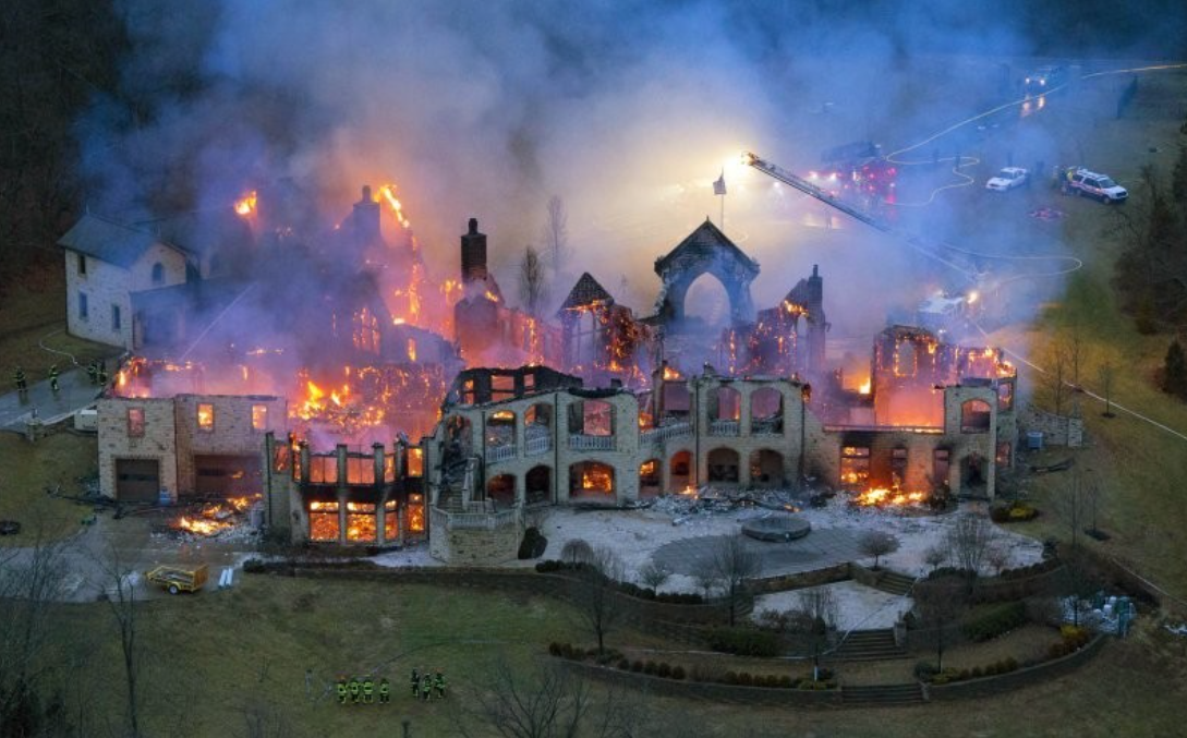 Požiar veľkej budovy so zrúcanými stenami, hasiči zasahujú. Dym stúpa, svetlá áut osvetľujú scénu.