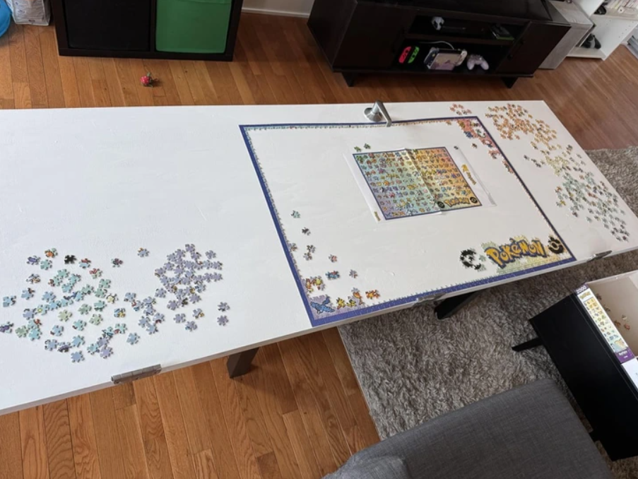 Rozostavané puzzle Pokémon na bielom stole v obývačke, okolo kúsok zloženej modrej hrany.