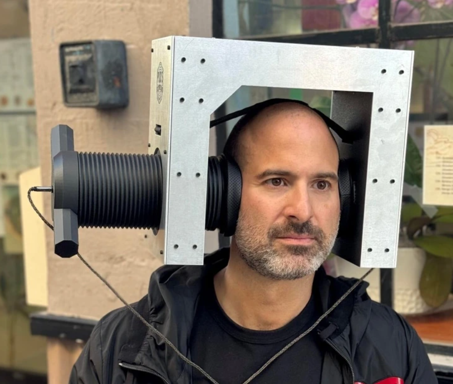 Muž s netradičnou konštrukciou na hlave stojí na ulici. Futuristický dizajn vyvoláva zvedavosť okoloidúcich.