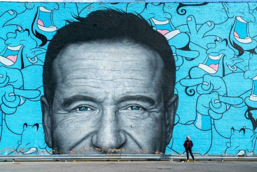 Nástenná maľba zobrazujúca detail tváre muža s modrou kresbou postáv v pozadí. Človek stojí pred umením.