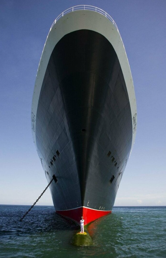 Veľká loď kotví na mori s mužom v bielom oblečení stojacim pod jej obrovskou provou.