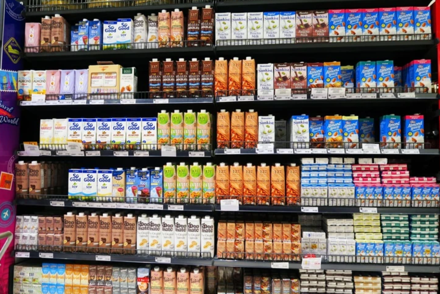 Regály supermarketu s rôznymi druhmi rastlinných mliek v kartónoch, vrátane mandľového a sójového.