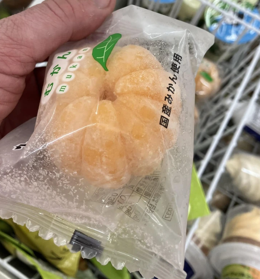 Zmrazená mandarínka v obale, japonský text na obale, držiak v ruke.